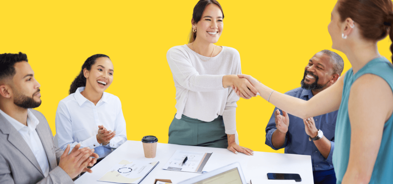 Two women shaking hands at a conference room table.